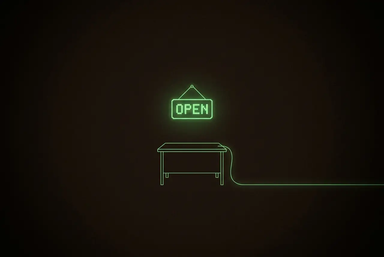a single desk in darkness with a glowing open sign above it